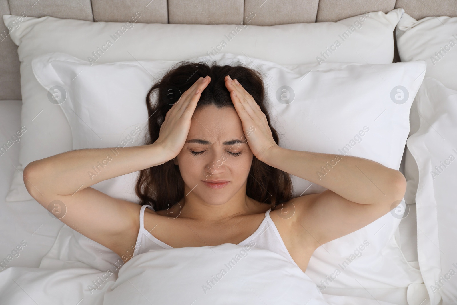 Photo of Woman suffering from headache in bed, top view