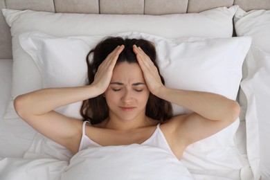 Photo of Woman suffering from headache in bed, top view