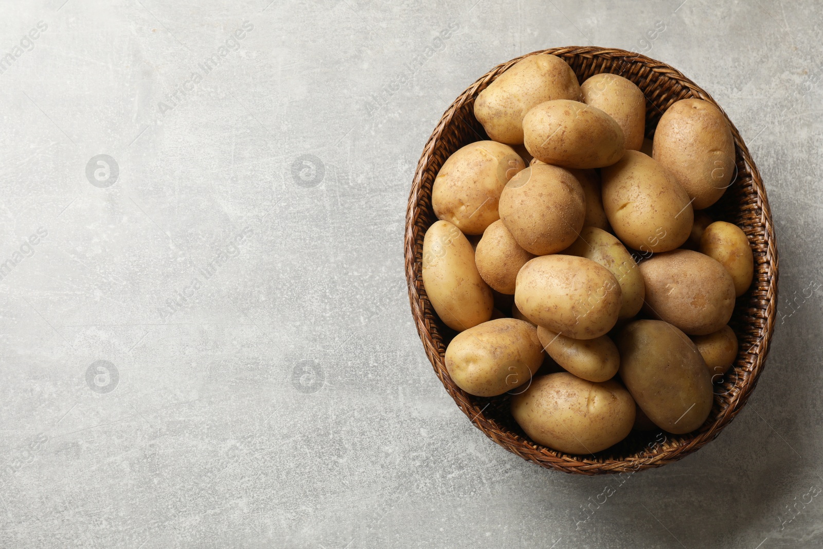 Photo of Many fresh potatoes in wicker basket on grey table, top view. Space for text