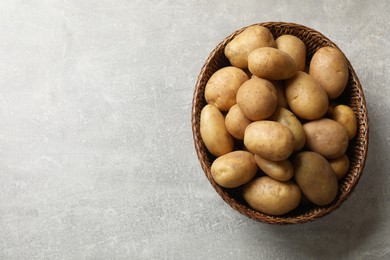 Photo of Many fresh potatoes in wicker basket on grey table, top view. Space for text