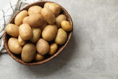 Photo of Many fresh potatoes in wicker basket on grey table, top view. Space for text