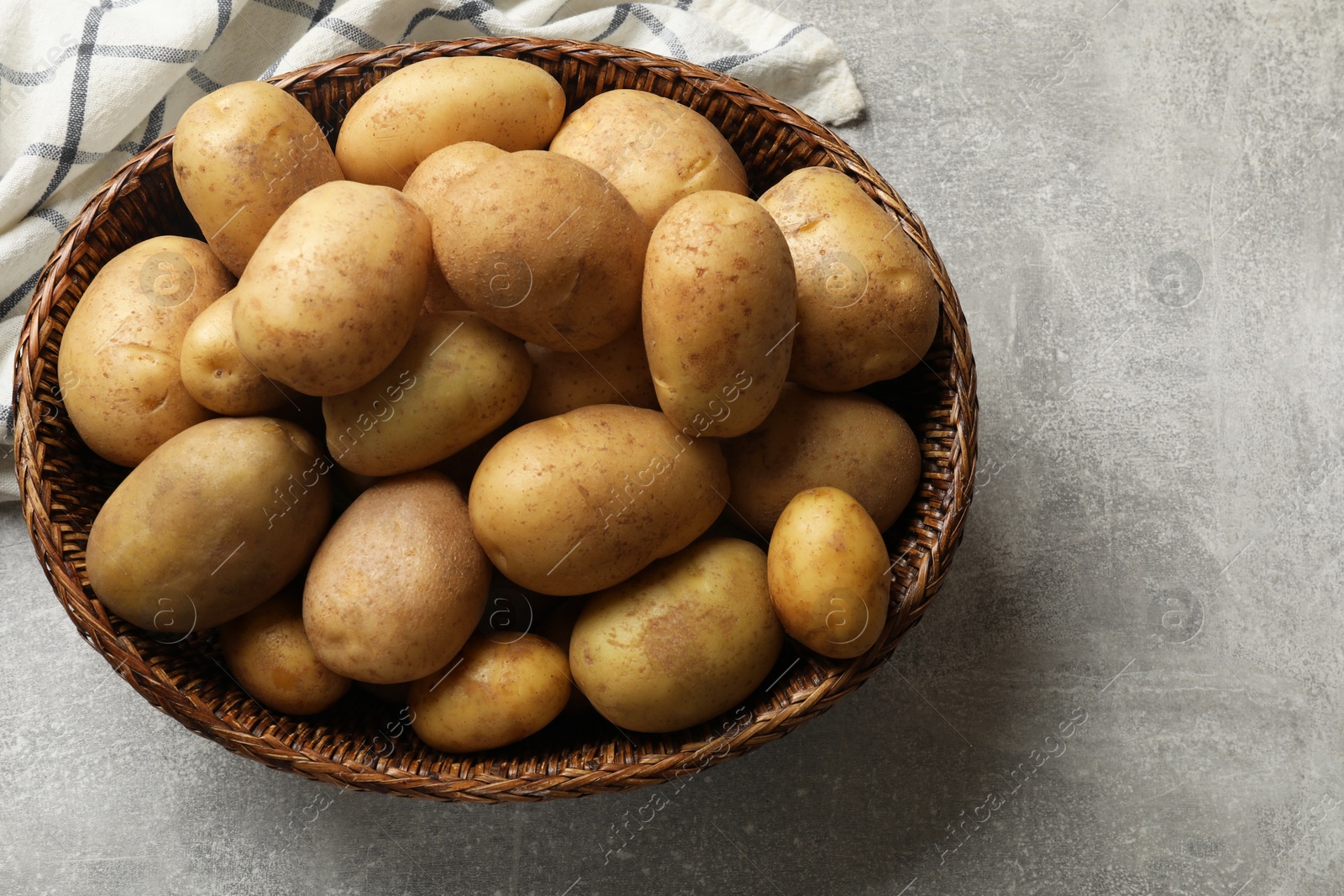 Photo of Many fresh potatoes in wicker basket on grey table, top view. Space for text