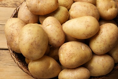 Photo of Many fresh potatoes in wicker basket on wooden table, closeup