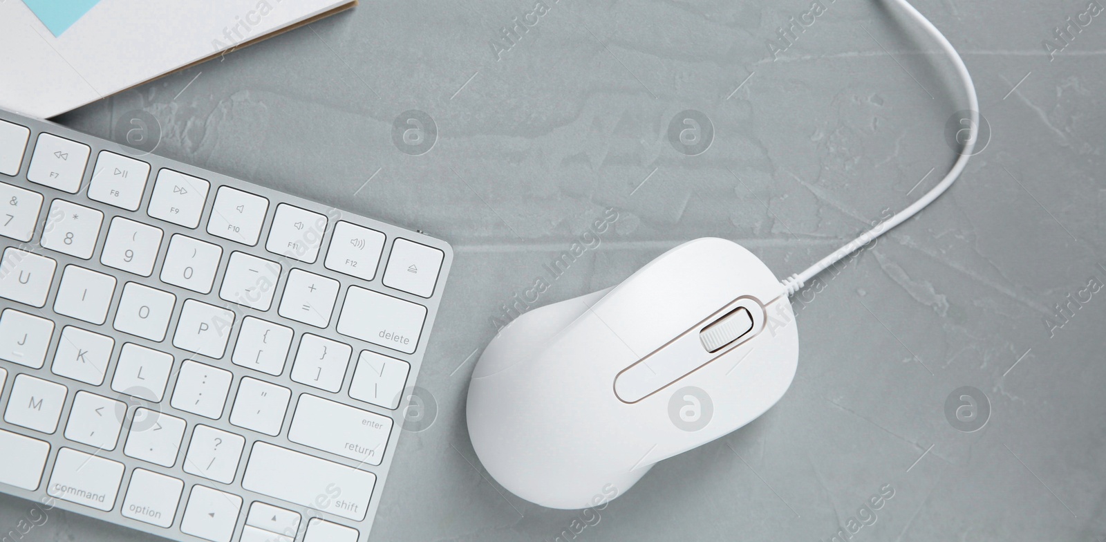 Photo of Wired mouse and computer keyboard on grey textured table, flat lay