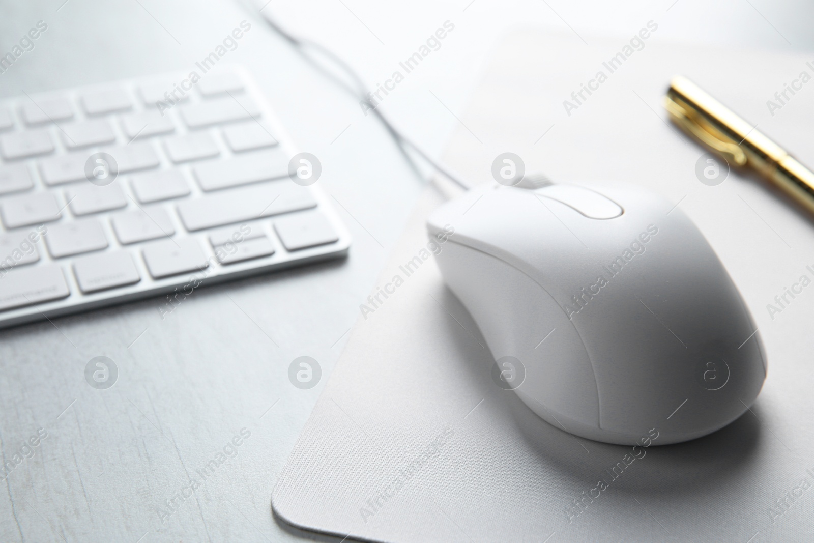 Photo of Wired mouse with mousepad and computer keyboard on light wooden table, closeup