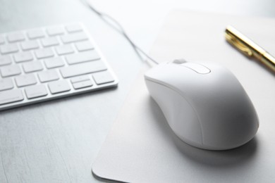 Wired mouse with mousepad and computer keyboard on light wooden table, closeup