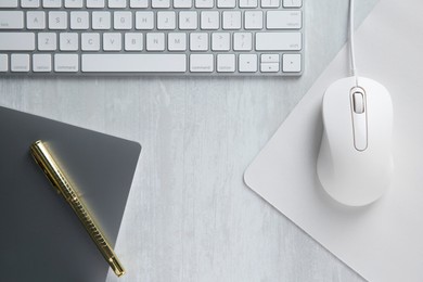 Photo of Wired mouse with mousepad, notebook, pen and computer keyboard on light wooden table, flat lay