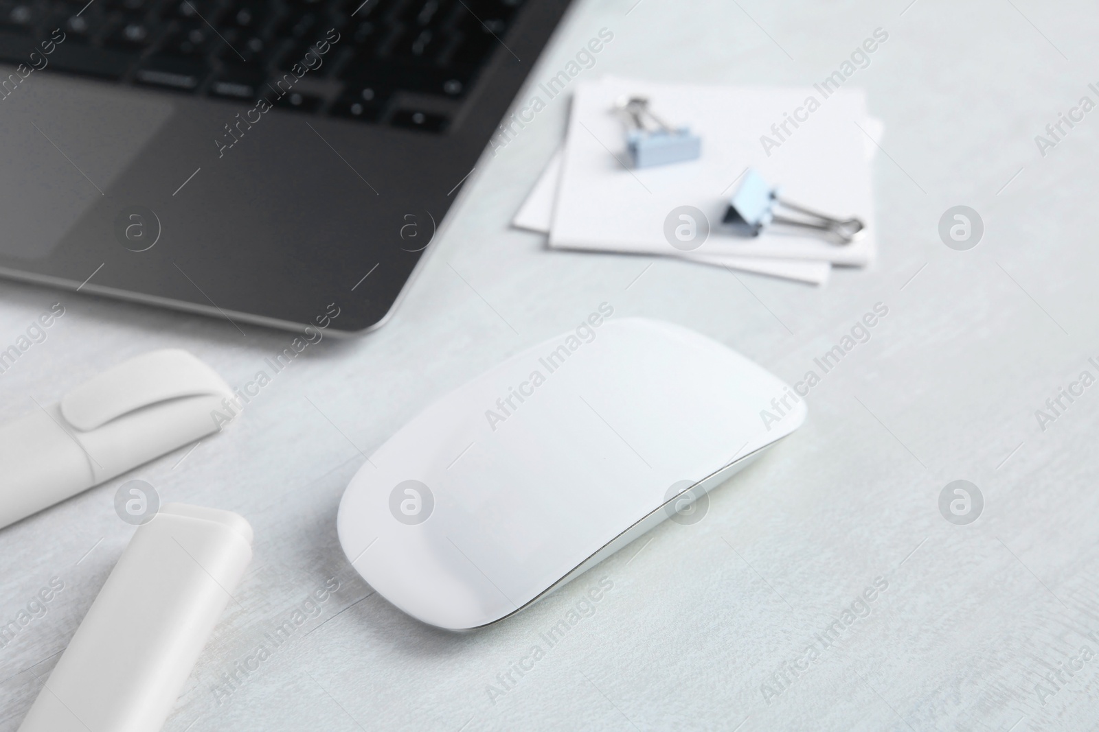 Photo of Wireless mouse, stationery and laptop on light wooden table, closeup