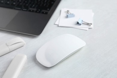 Photo of Wireless mouse, stationery and laptop on light wooden table, closeup