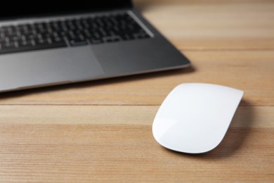 Wireless mouse and laptop on wooden table, closeup