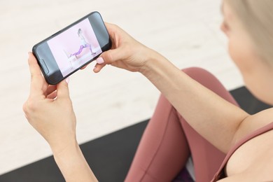 Online fitness trainer. Woman watching tutorial on smartphone indoors, above view