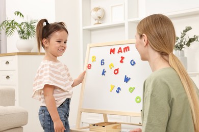 Mom teaching her daughter alphabet with magnetic letters at home