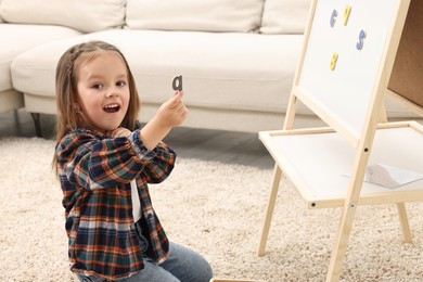 Photo of Cute little girl putting magnetic letters on board at home. Learning alphabet