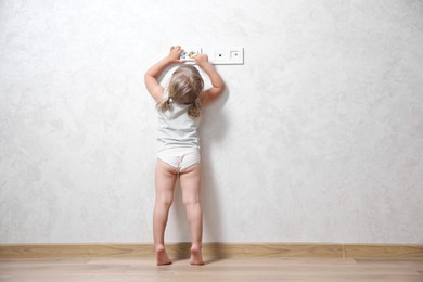 Little child playing with electrical socket indoors, back view. Dangerous situation
