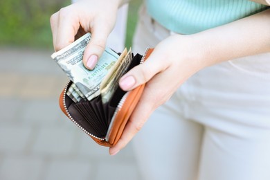 Photo of Woman holding purse with banknotes outdoors, closeup