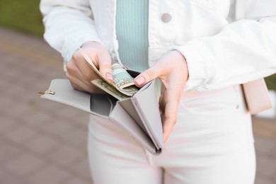 Woman holding purse with banknotes outdoors, closeup