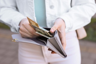 Photo of Woman holding purse with banknotes outdoors, closeup