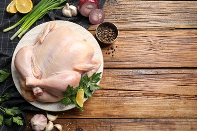 Fresh raw chicken with different products on wooden table, flat lay. Space for text