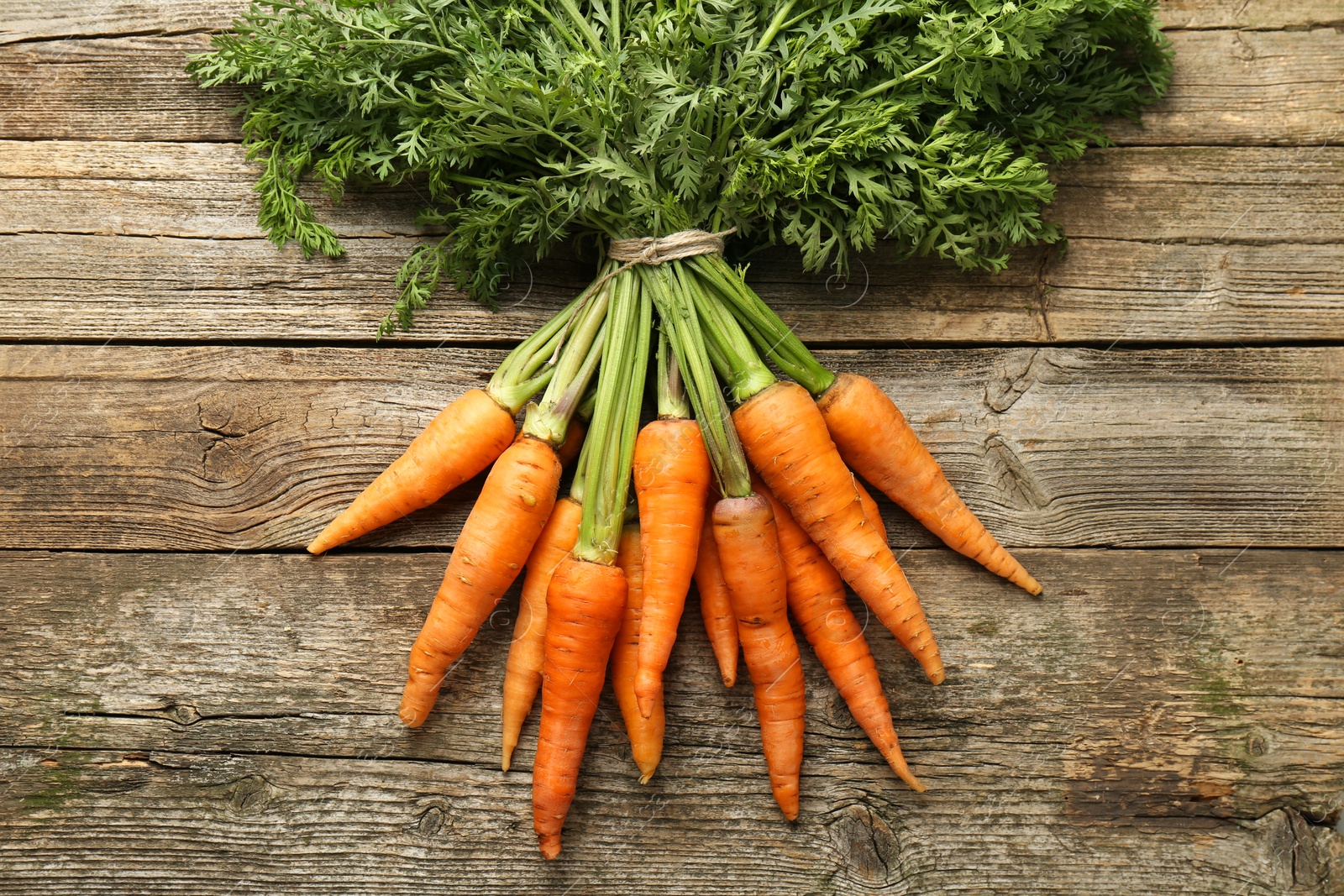 Photo of Bunch of tasty ripe juicy carrots on wooden table, top view