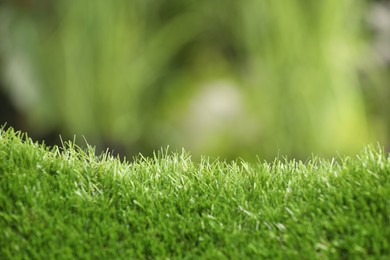 Green artificial grass against blurred background, closeup