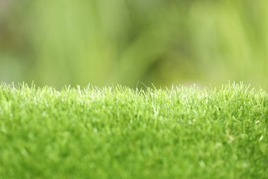 Green artificial grass against blurred background, closeup