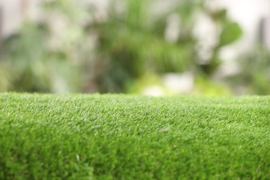 Green artificial grass against blurred background, closeup