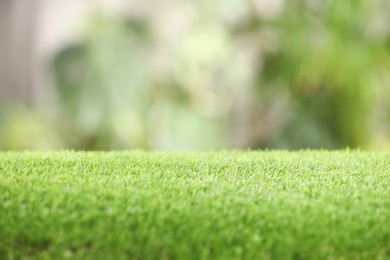 Green artificial grass against blurred background, closeup