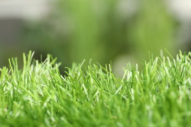 Green artificial grass against blurred background, closeup