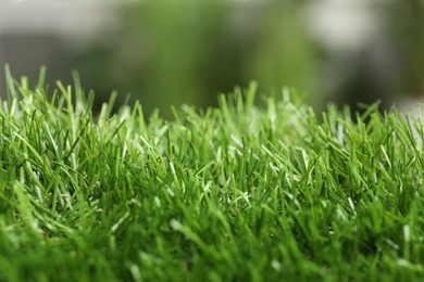 Green artificial grass against blurred background, closeup