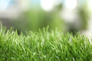 Green artificial grass against blurred background, closeup