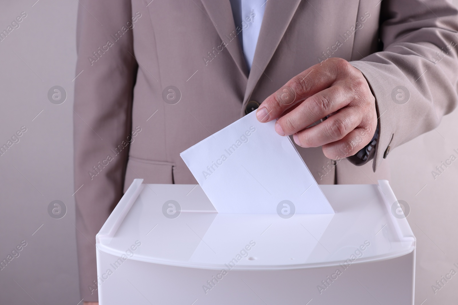 Photo of Man putting his vote into ballot box against light grey background, closeup