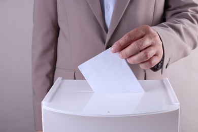 Photo of Man putting his vote into ballot box against light grey background, closeup