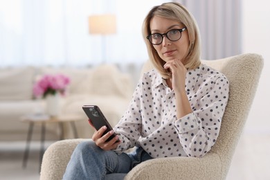Woman with glasses using mobile phone at home, space for text
