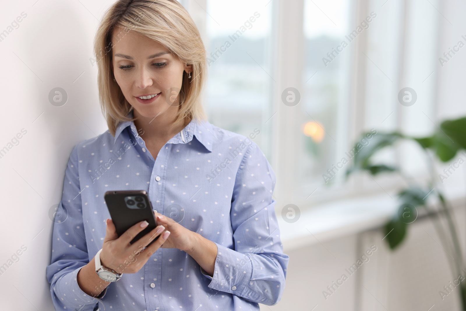 Photo of Happy woman using mobile phone near window indoors, space for text