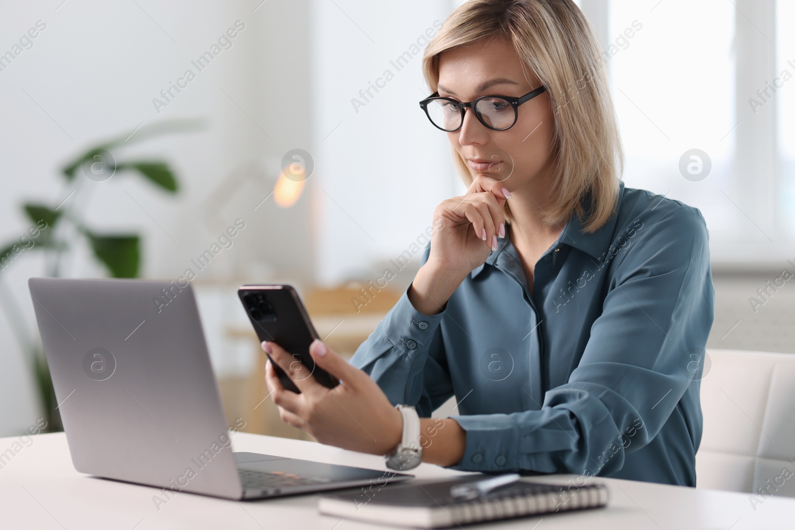 Photo of Woman using mobile phone at white table indoors