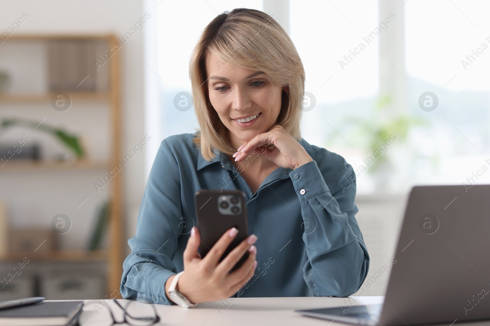 Photo of Happy woman using mobile phone at white table indoors