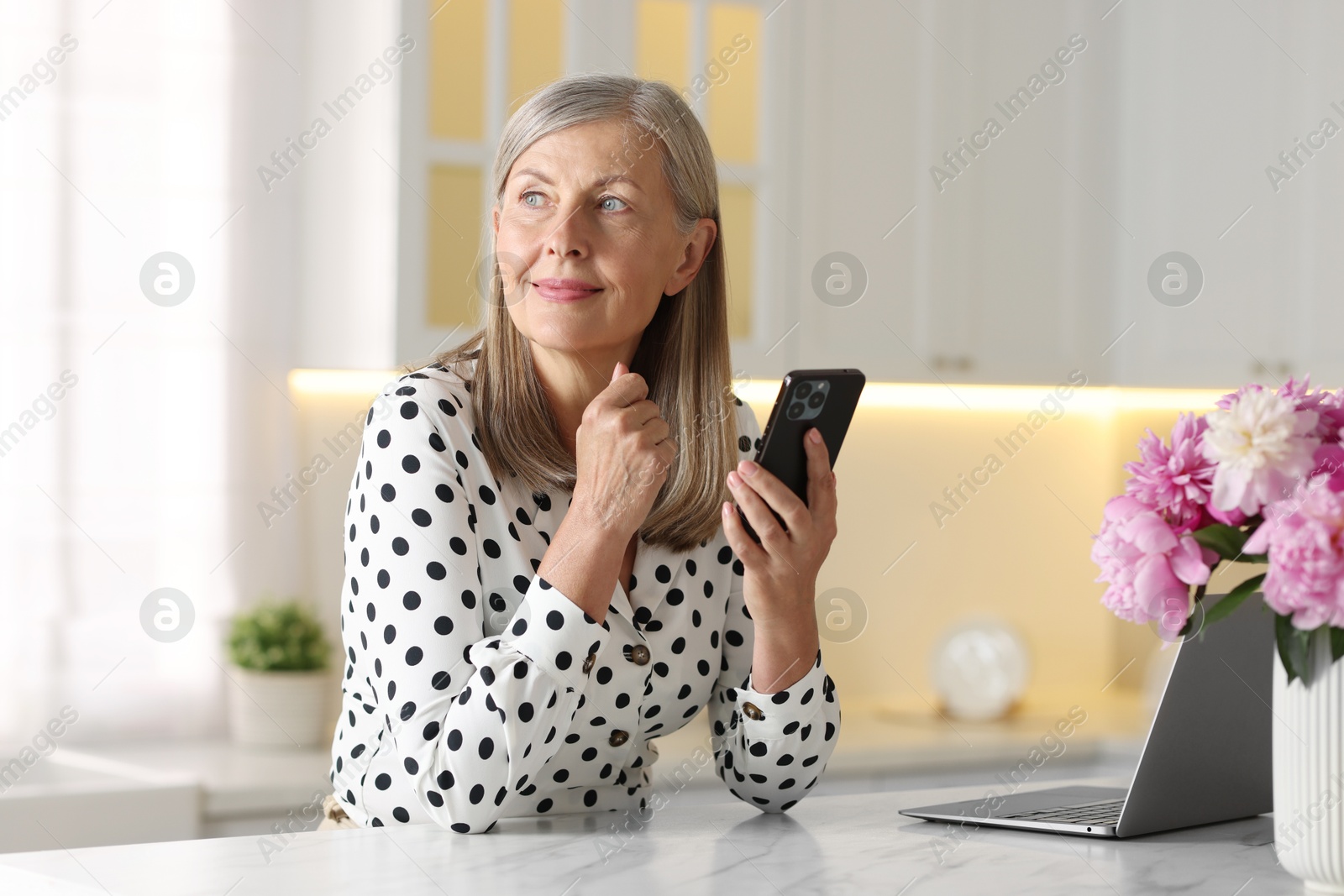 Photo of Senior woman using mobile phone at white table indoors