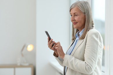 Senior woman using mobile phone at home, space for text