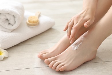 Woman applying moisturizing cream onto her feet on floor, closeup. Body care