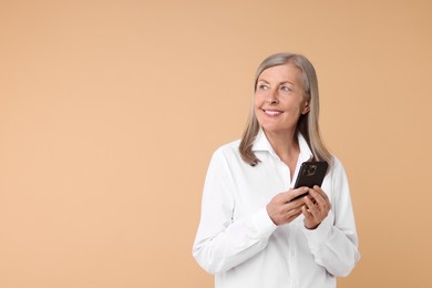 Senior woman with phone on beige background, space for text