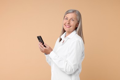 Senior woman with phone on beige background