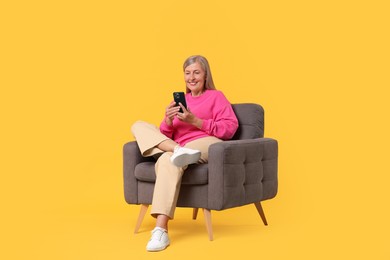 Senior woman with phone on armchair against orange background