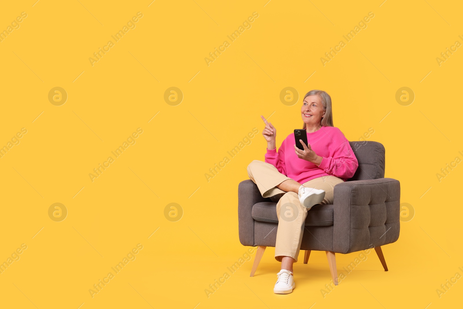 Photo of Senior woman with phone on armchair against orange background, space for text