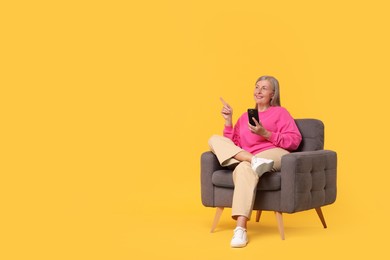 Photo of Senior woman with phone on armchair against orange background, space for text