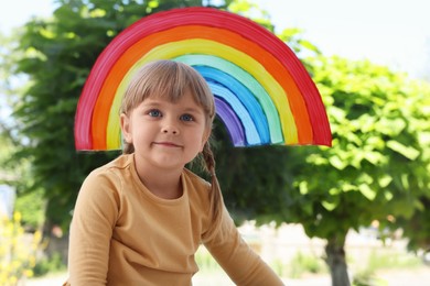 Little girl near rainbow painting on window indoors