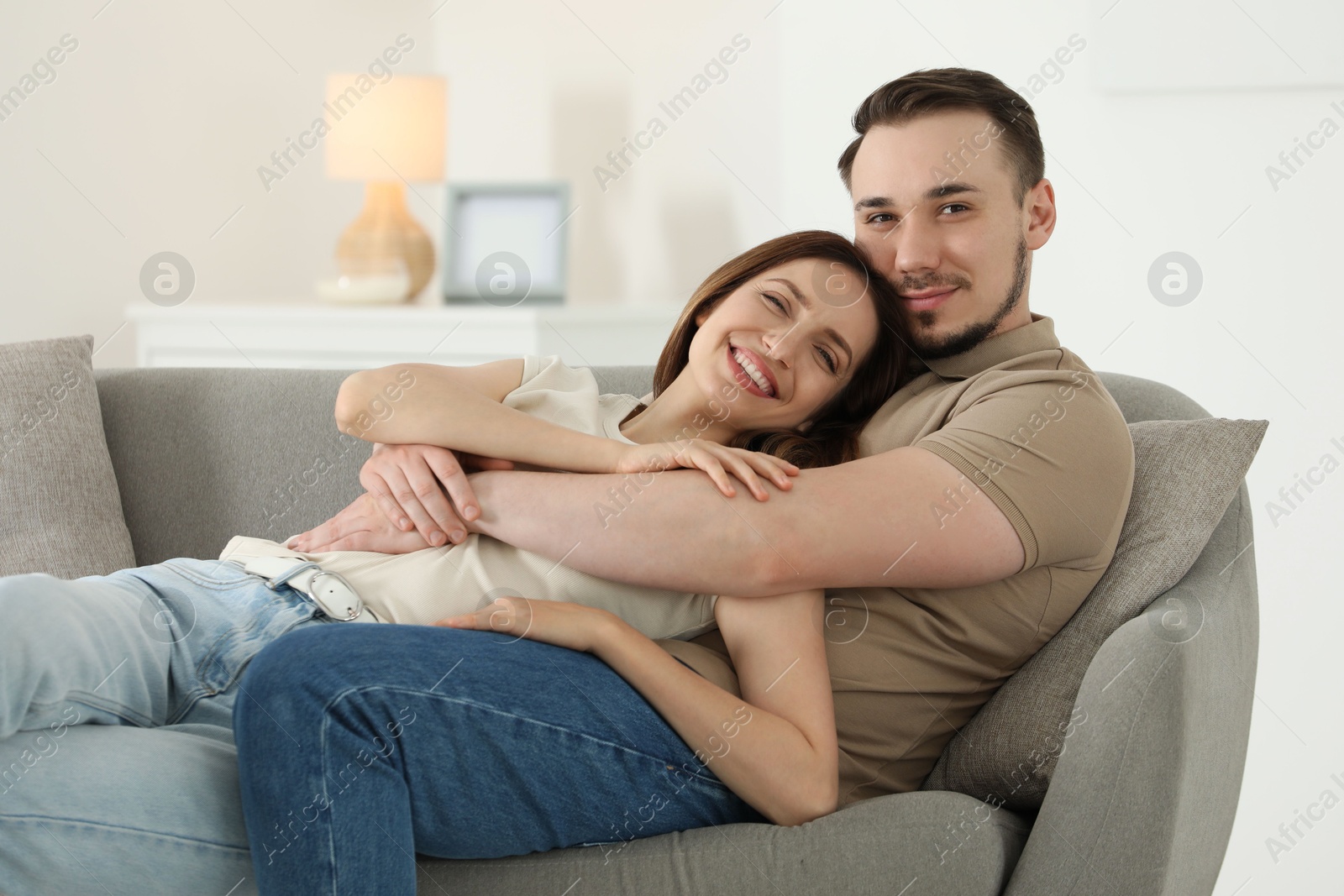 Photo of Man hugging his happy girlfriend on sofa at home