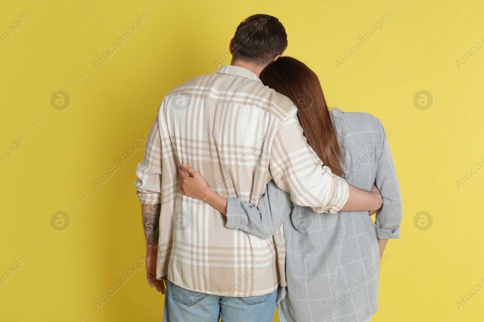 Photo of Cute couple hugging on yellow background, back view