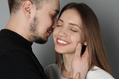 Photo of Man hugging and kissing his happy girlfriend on grey background