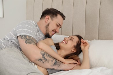 Photo of Man hugging his happy girlfriend on bed at home