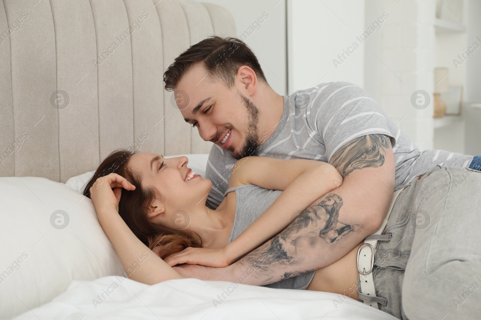 Photo of Man hugging his happy girlfriend on bed at home